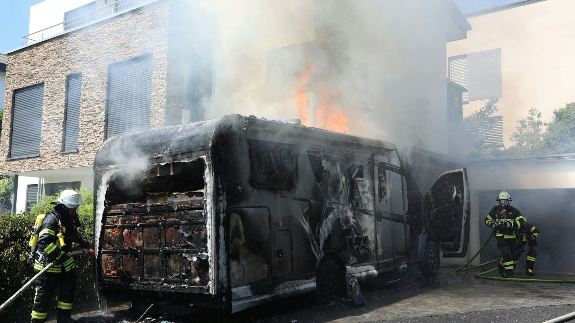 Feuerwehrleute löschen ein Wohnmobil, die Flammen schlagen aus dem Dach des Fahrzeugs.
