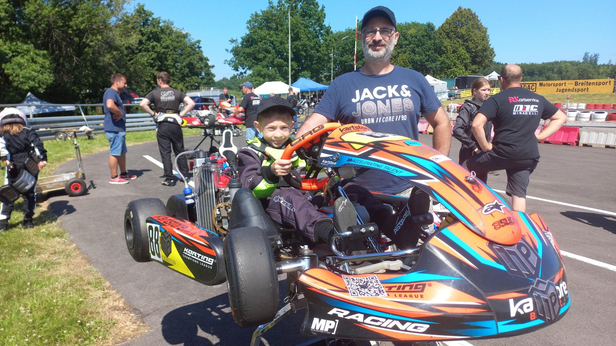 Ein Vater steht neben einem aufgebockten Kart, in dem sein siebenjähriger Sohn sitzt.