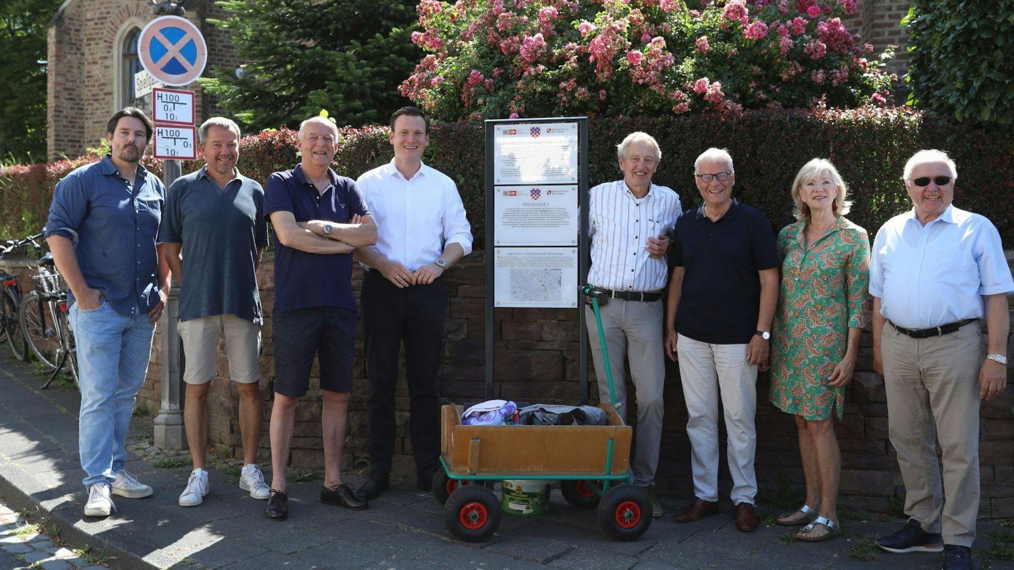 Sieben Männer und eine Frau neben einer Stele mit Info-Tafeln.