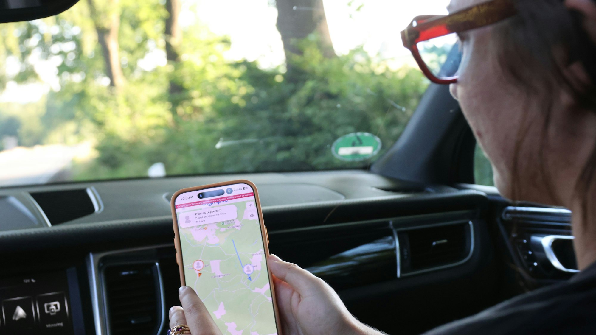 Eine Frau sitzt auf dem Beifahrersitz in einem Auto und schaut auf das Handy und eine Navigations-App.