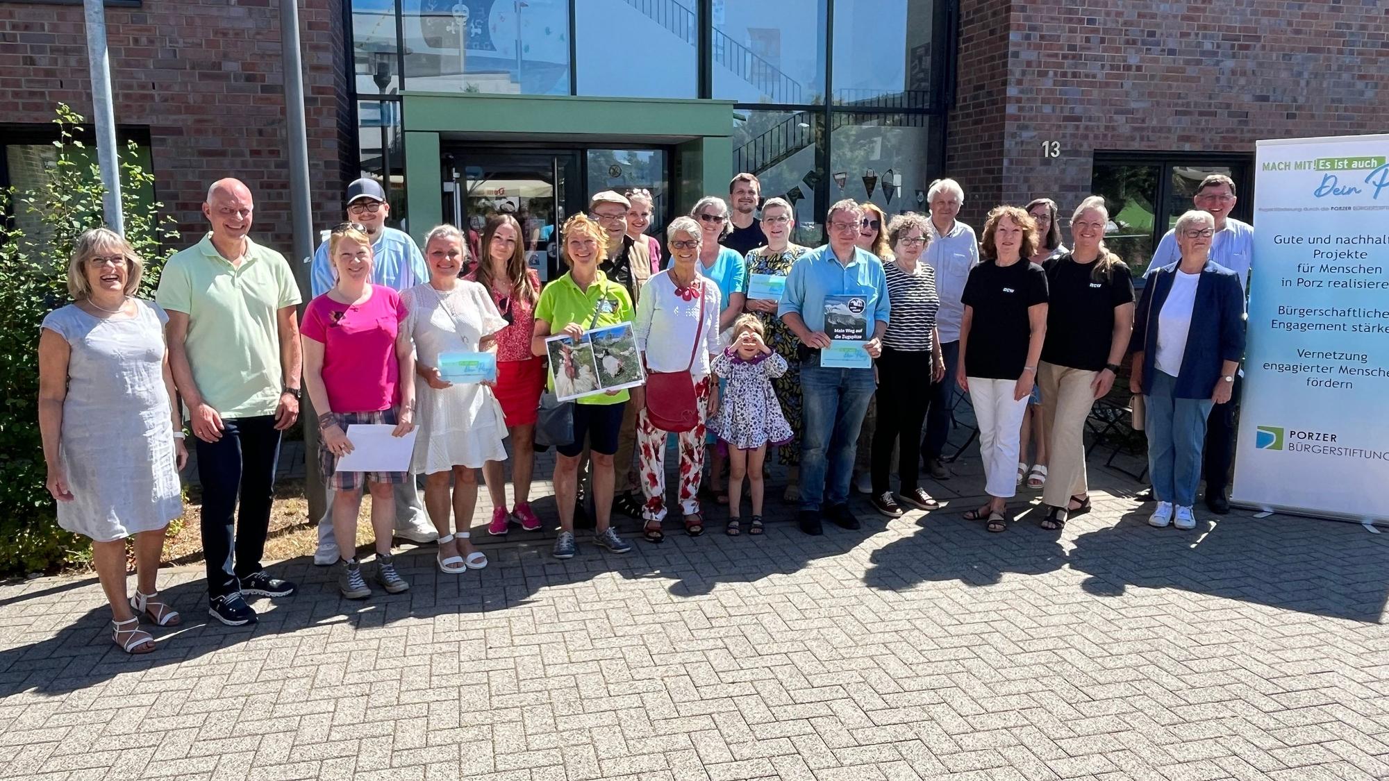 Viele Menschen stehen im Halbkreis vor einem Gebäude mit einer gläsernen Eingangstür.