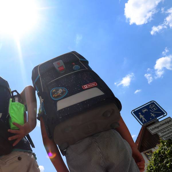 Zwei Kinder laufen mit ihren Büchertaschen im Sonnenschein.