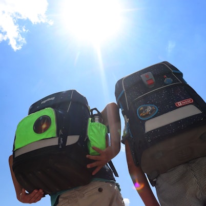 Zwei Kinder laufen mit ihren Büchertaschen im Sonnenschein.