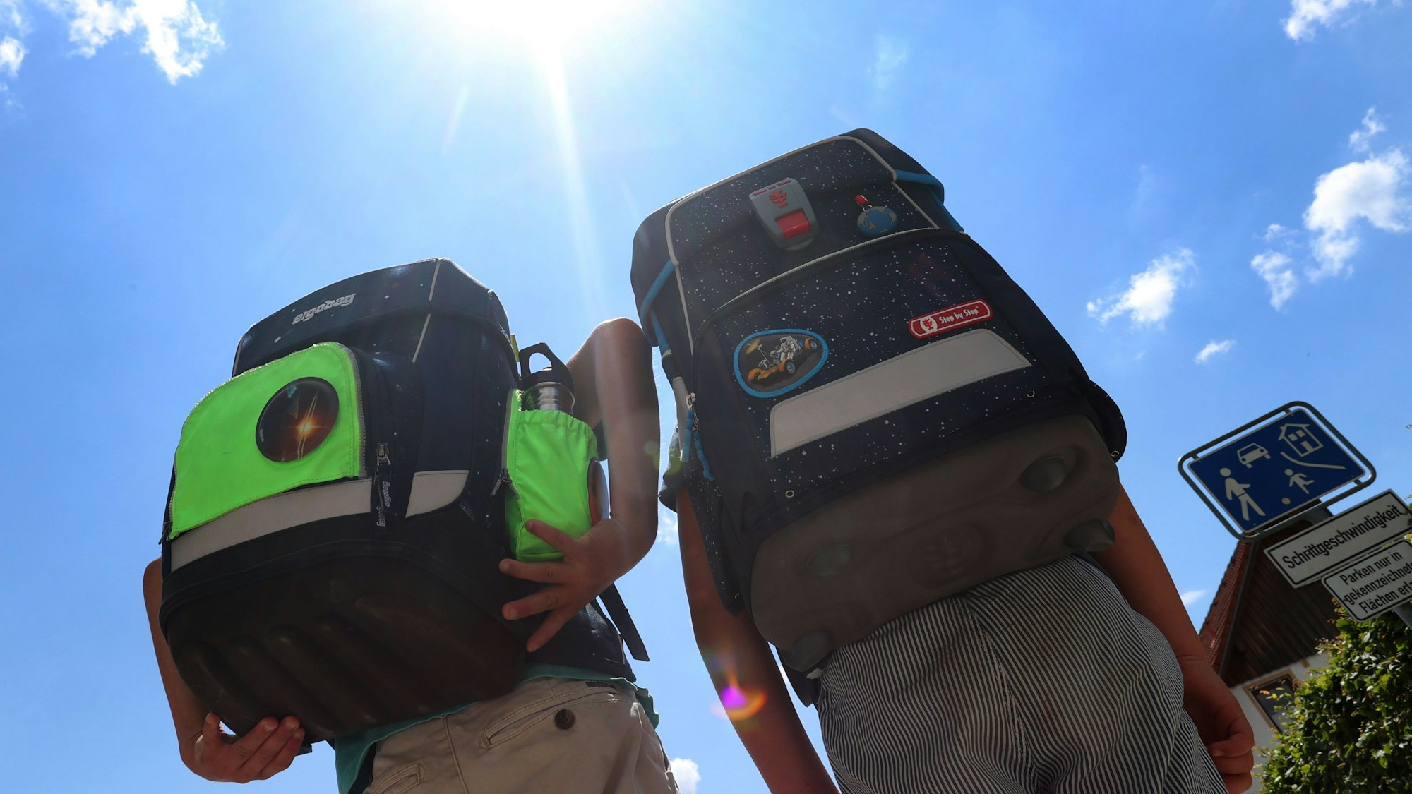 Zwei Kinder laufen mit ihren Büchertaschen im Sonnenschein.
