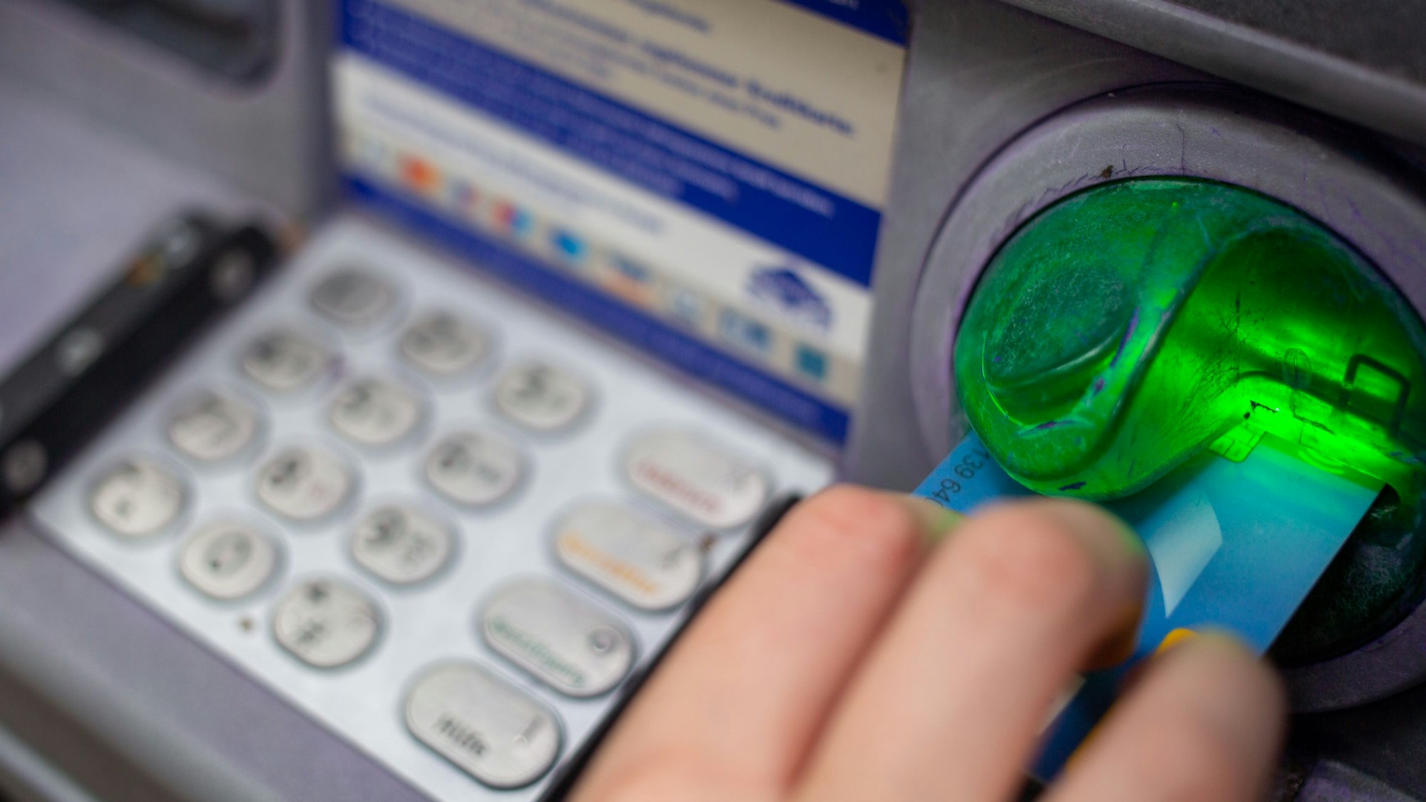 Ein Bankkunde steckt eine Girokarte in einen Geldautomaten.