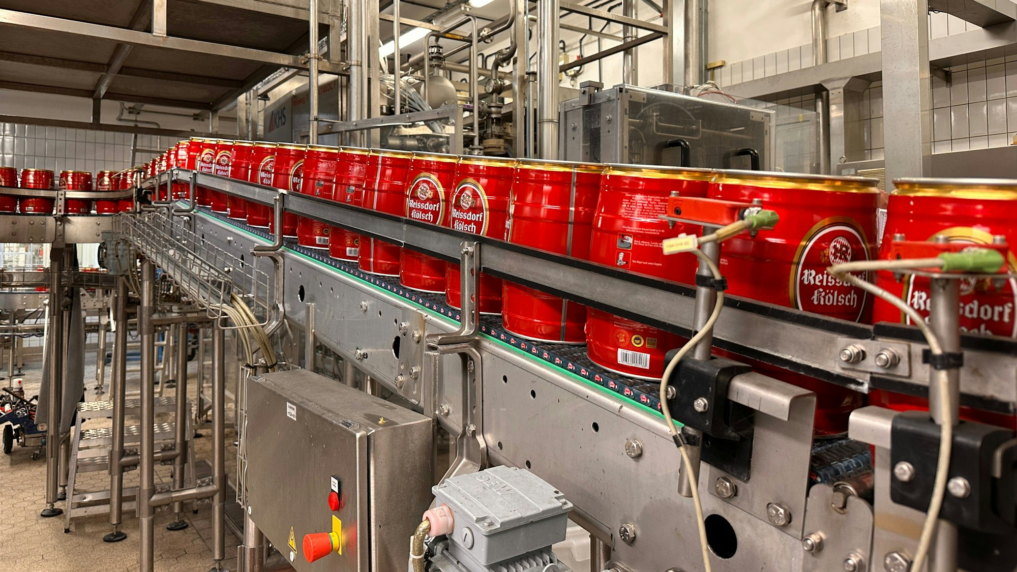 Über eine Förderband mit Waschfunktion laufen rote Reissdorf-Fässer.