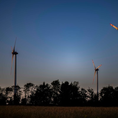 Das Bild zeigt drei Windräder, im Vordergrund Bäume.