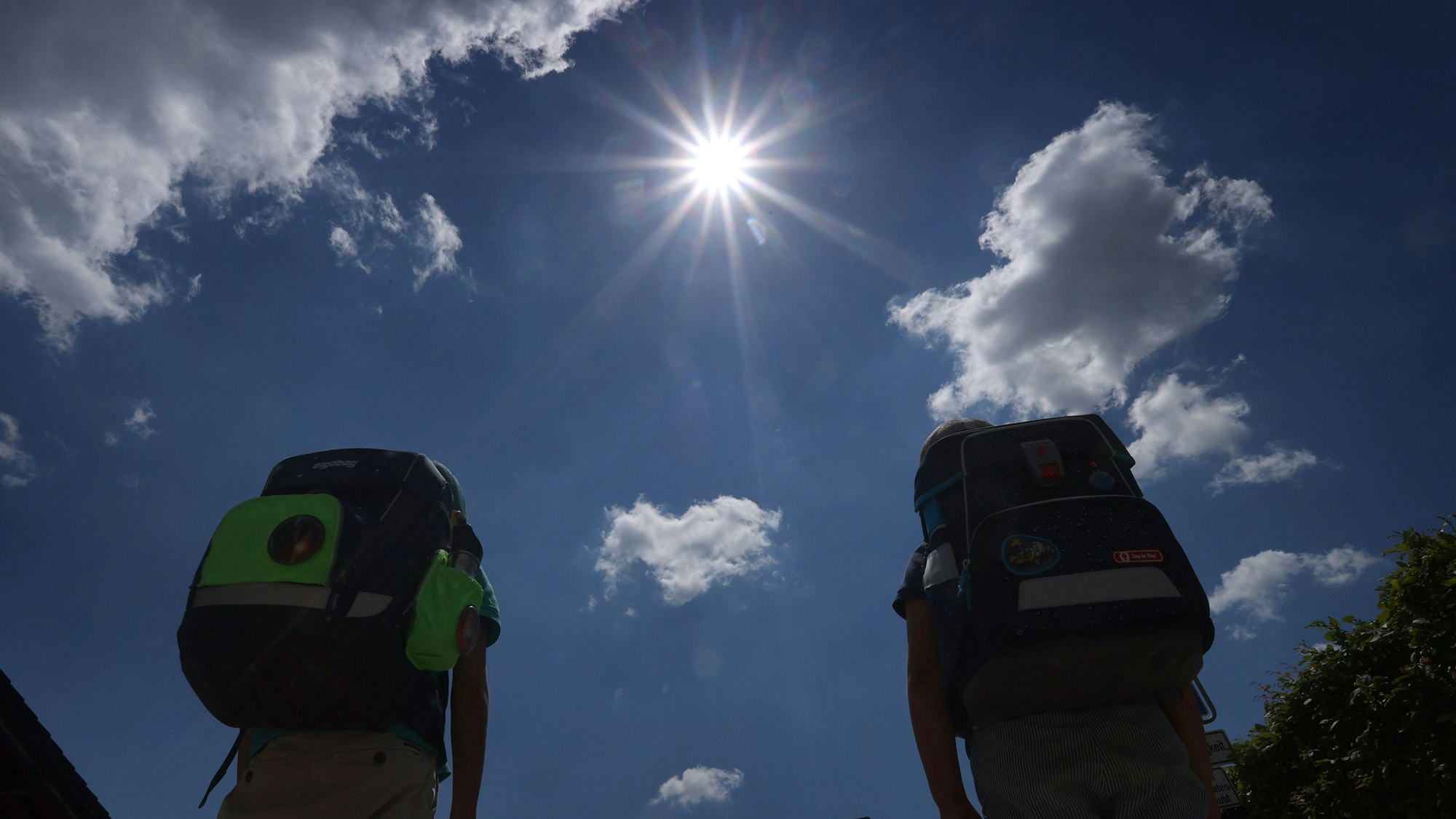 Zwei Kinder laufen mit ihren Büchertaschen im Sonnenschein. Viele Schülerinnen und Schüler haben derzeit Hitzefrei. (Archivbild)