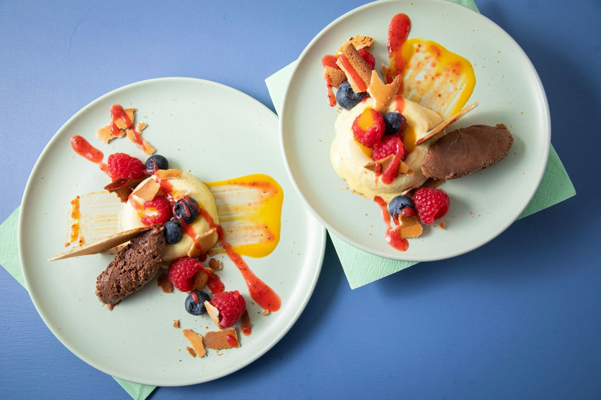 Sieht aus wie ein Bagel aus Eis: In sogenannte Savarin-Formen wird das Mangoeis gefüllt und gefroren. Die Mitte wird mit Fruchtigem gefüllt, dazu einen Klecks Schokoladenmousse, Mango- und Erdbeerpüree drunter und drüber streichen.