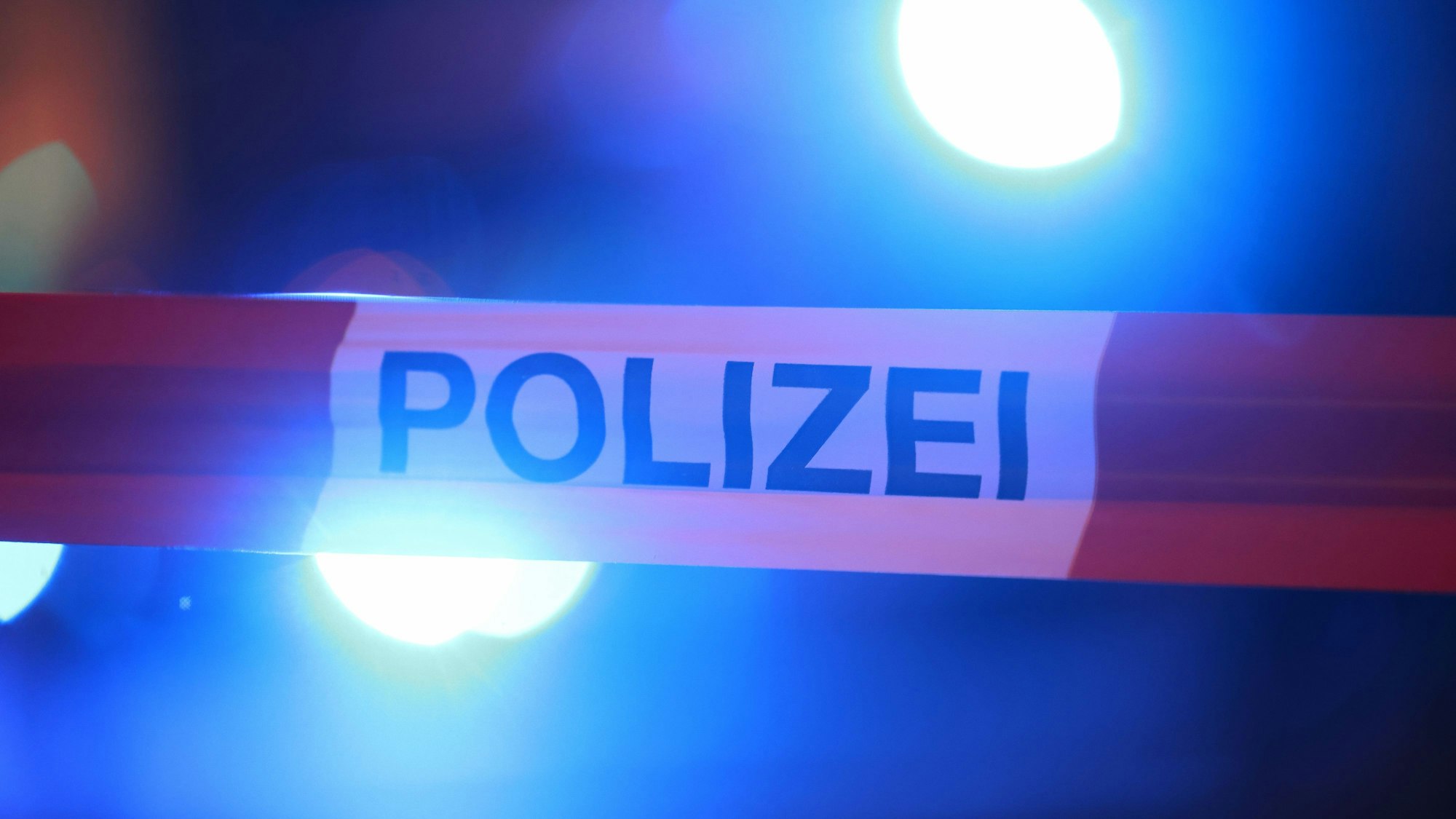 Blaulichter leuchten hinter einem Absperrband der Polizei. (Symbolbild)