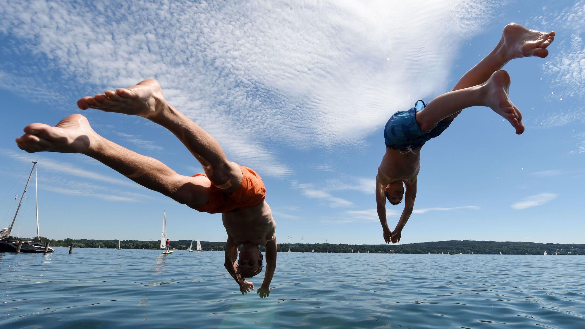 Zwei junge Männer springen in einen See.