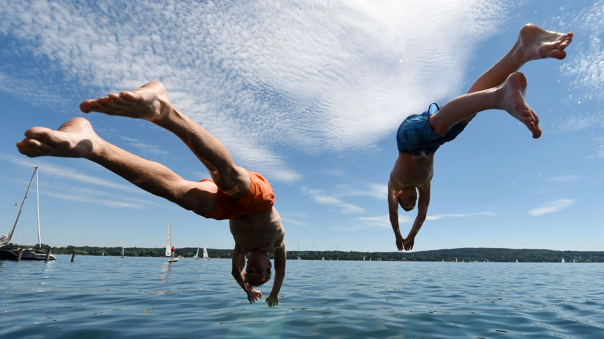 Zwei junge Männer springen in einen See.