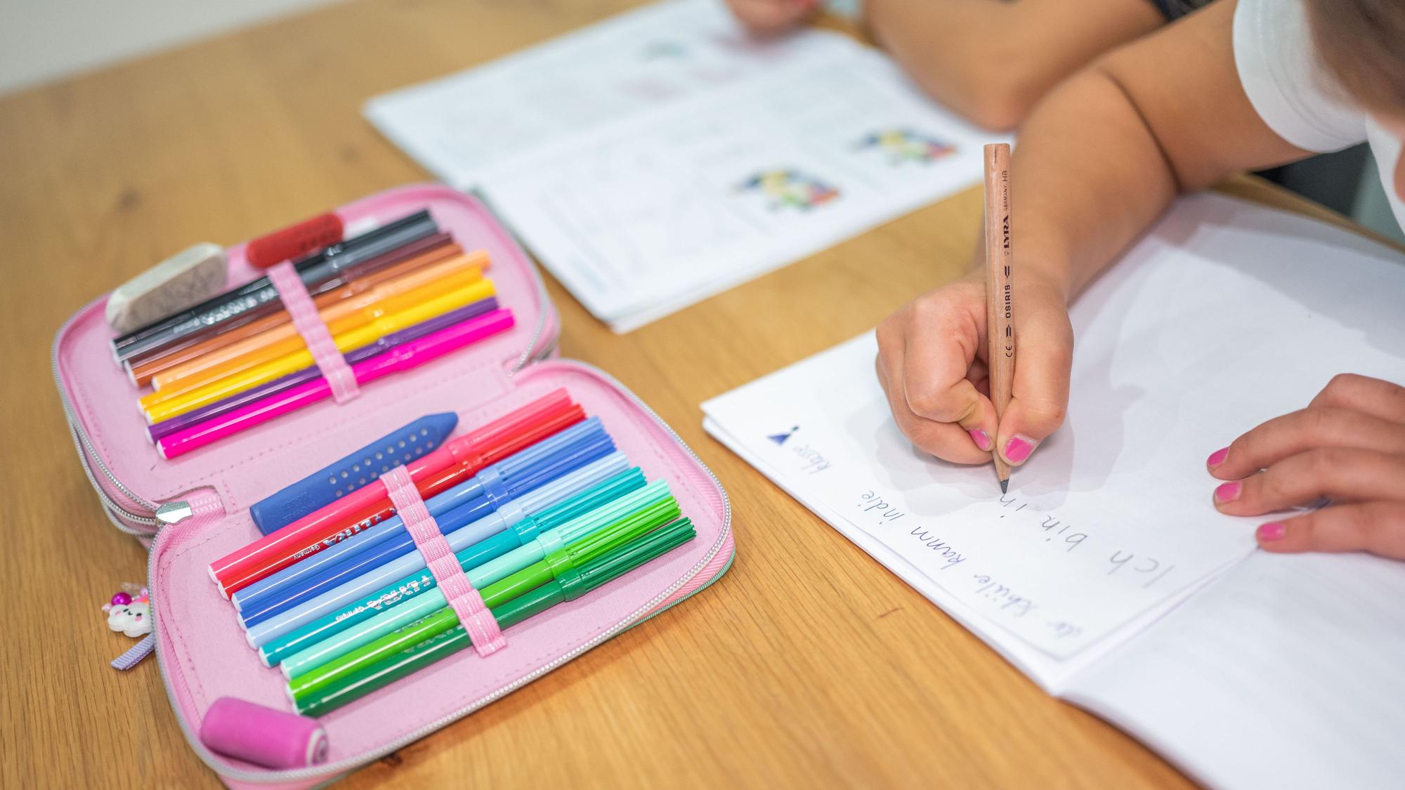 Grundschüler sitzen an einem Tisch und erledigen Schulaufgaben.