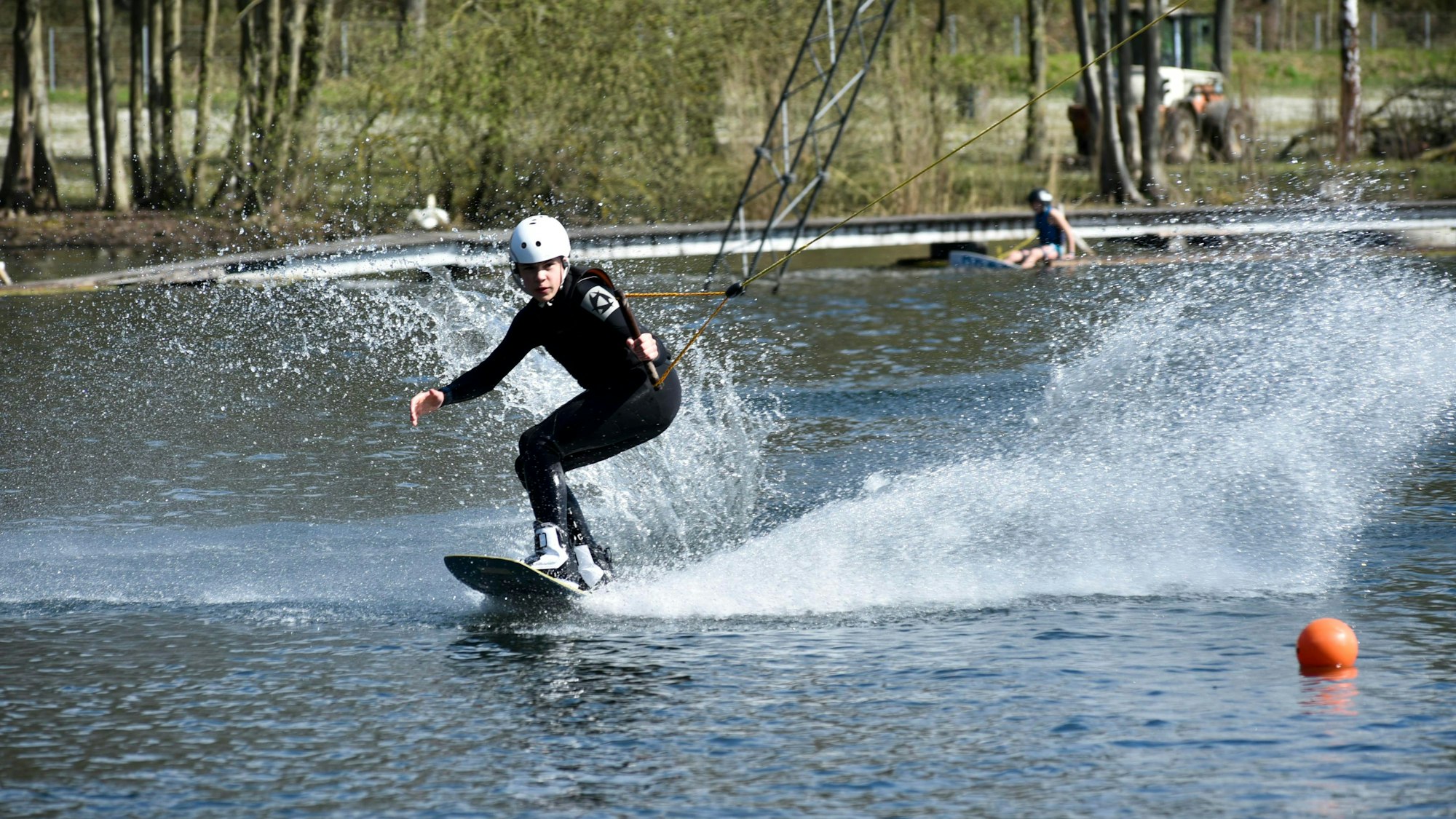 Ein junger Mann steht auf einem Board und gleitet über das Wasser während er sich an einem Trapez festhält.