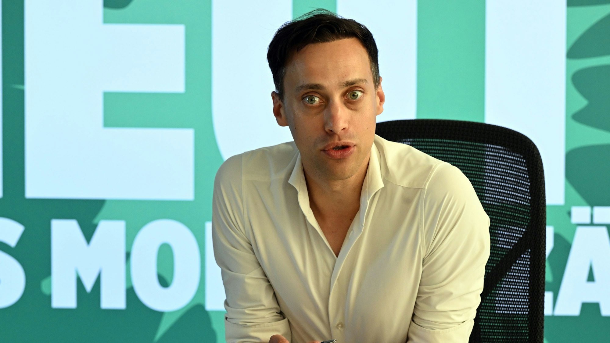 Tim Achtermeyer, Landesvorsitzender, sitzt vor einem Plakat für die Kommunalwahl im September 2025.