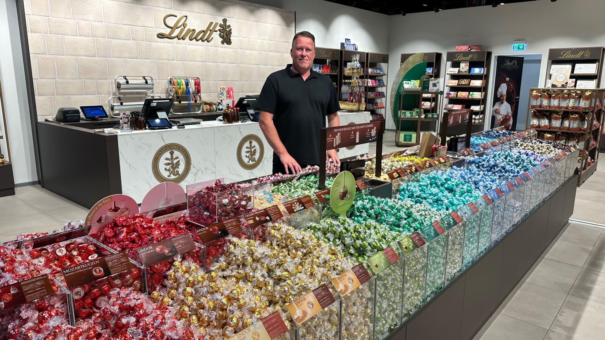Storemanager Sascha Leeser in seinem Lindt-Shop. In den bunten Farben des Regenbogens sind süßen Versuchungen in der Ladenmitte angeordnet.