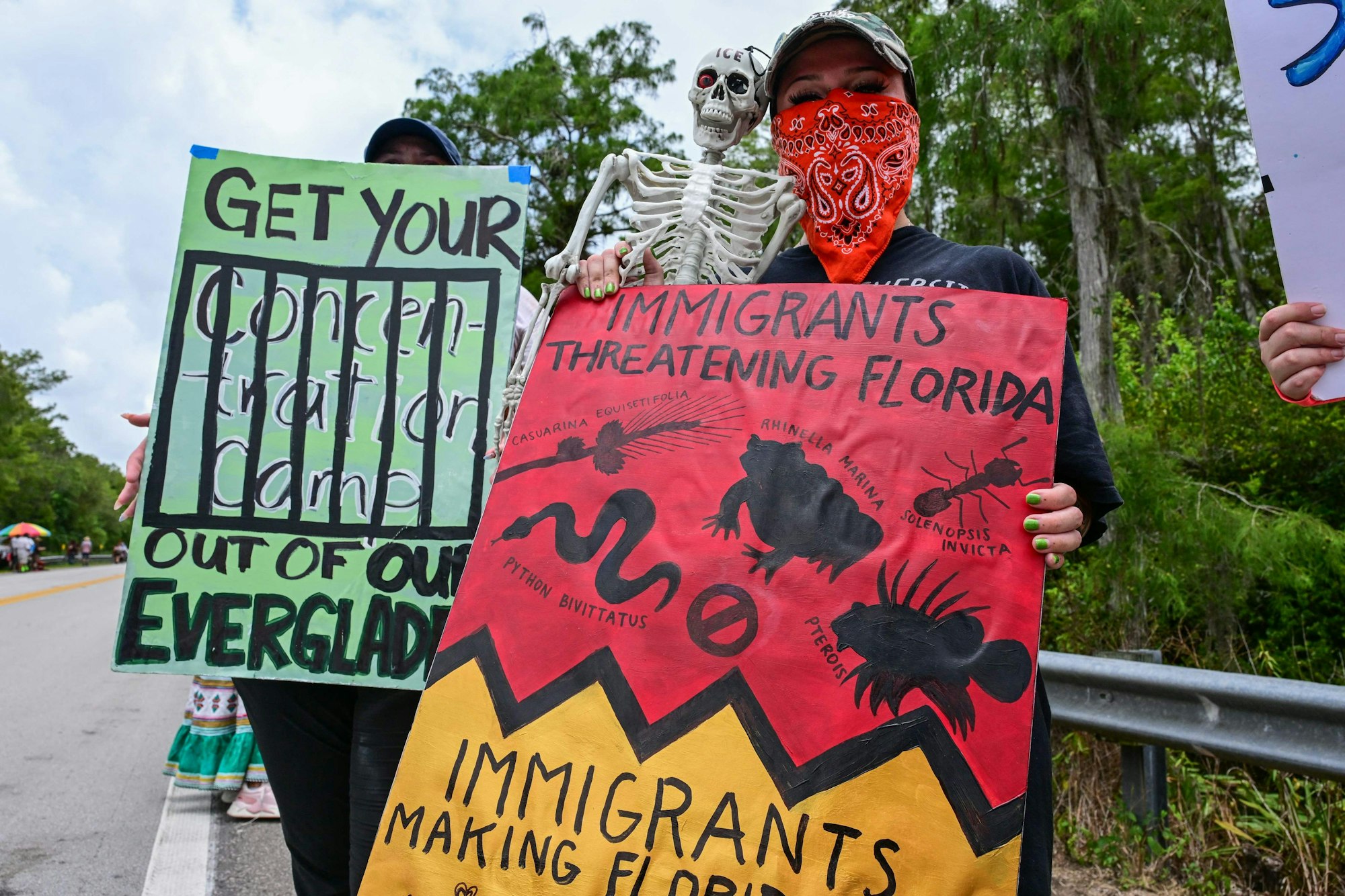EDITORS NOTE: Graphic content / Demonstrators hold signs as they protest the construction of an immigrant detention center, dubbed "Alligator Alcatraz," in the Everglades near Ochopee, Florida, on June 28, 2025. Florida began construction this week on a detention center surrounded by fierce reptiles and cypress swamps, an "Alligator Alcatraz" in the Everglades wetlands, as part of US President Donald Trump's expansion of deportations of undocumented migrants. The chosen site, an abandoned airfield in the heart of a sprawling network of mangrove forests, imposing marshes and "rivers of grass" that form the conservation area, will house large tents and beds for 1,000 "criminal aliens," according to state Attorney General James Uthmeier. (Photo by GIORGIO VIERA / AFP)