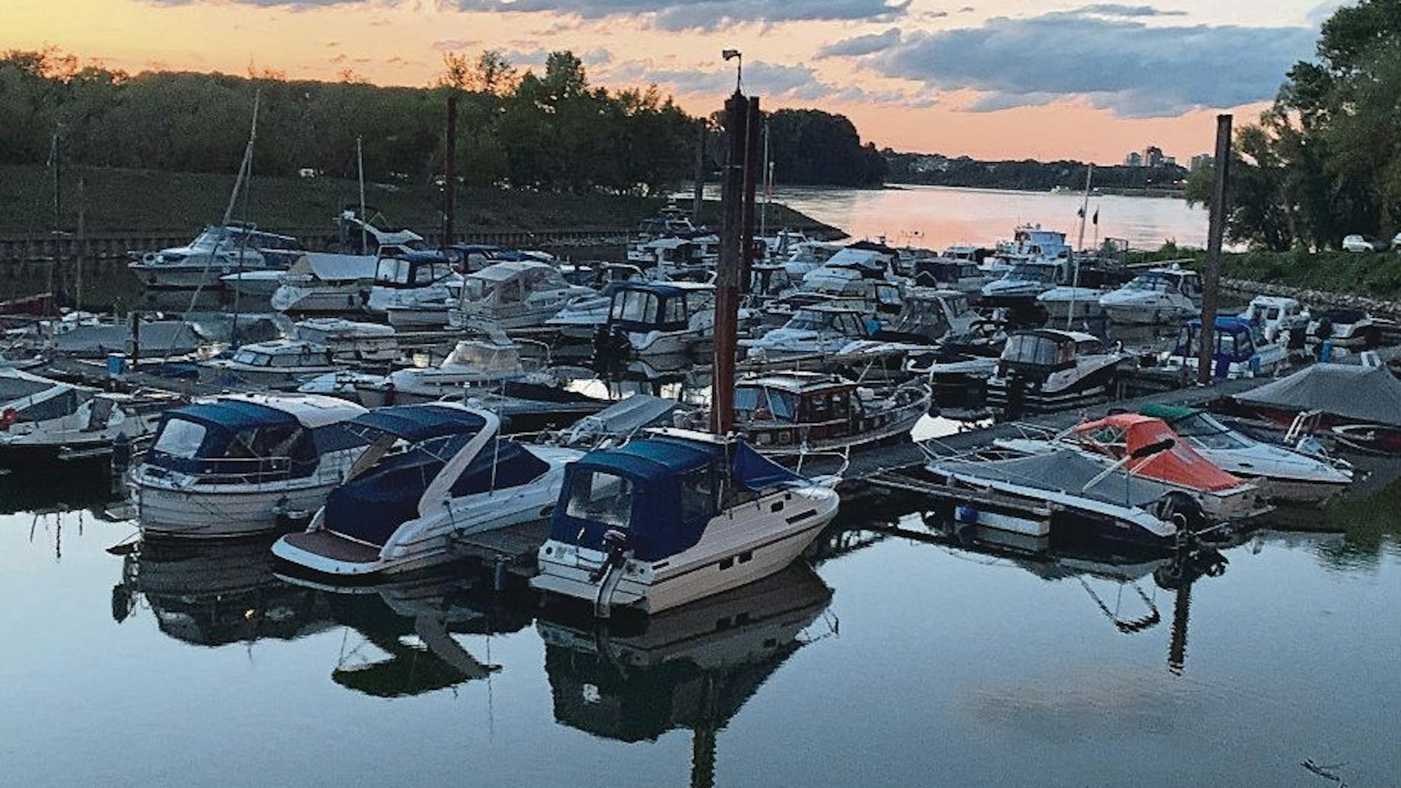 Mehrere Boote liegen in einem kleinen Hafen, im Hintergrund geht die Sonne unter.