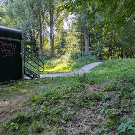 Ein Deich und ein Aufgang zu einer Brücke liegen in einem Wald.