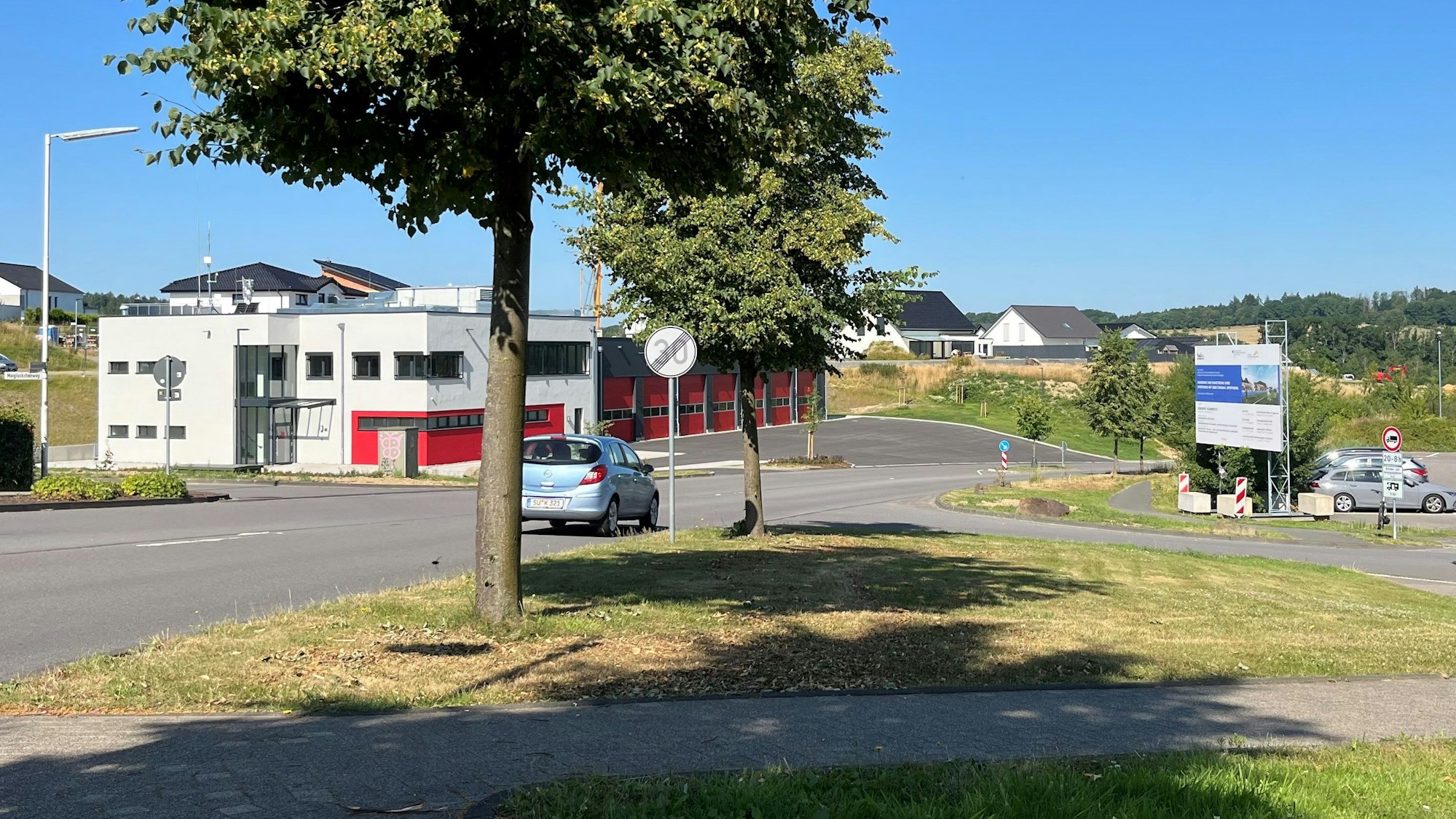 Der geplante Kreisverkehr soll zwischen der Zufahrt zum Parkplatz (rechts) und der Einmündung Maiglöckchenweg in die Gouvieuxstraße (links) gebaut werden. Das Gebäude im Bild ist das neue Feuerwehrhaus.