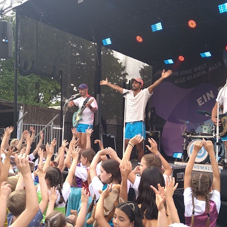 Drei Männer stehen auf der Bühne und singen und spielen Gitarre.