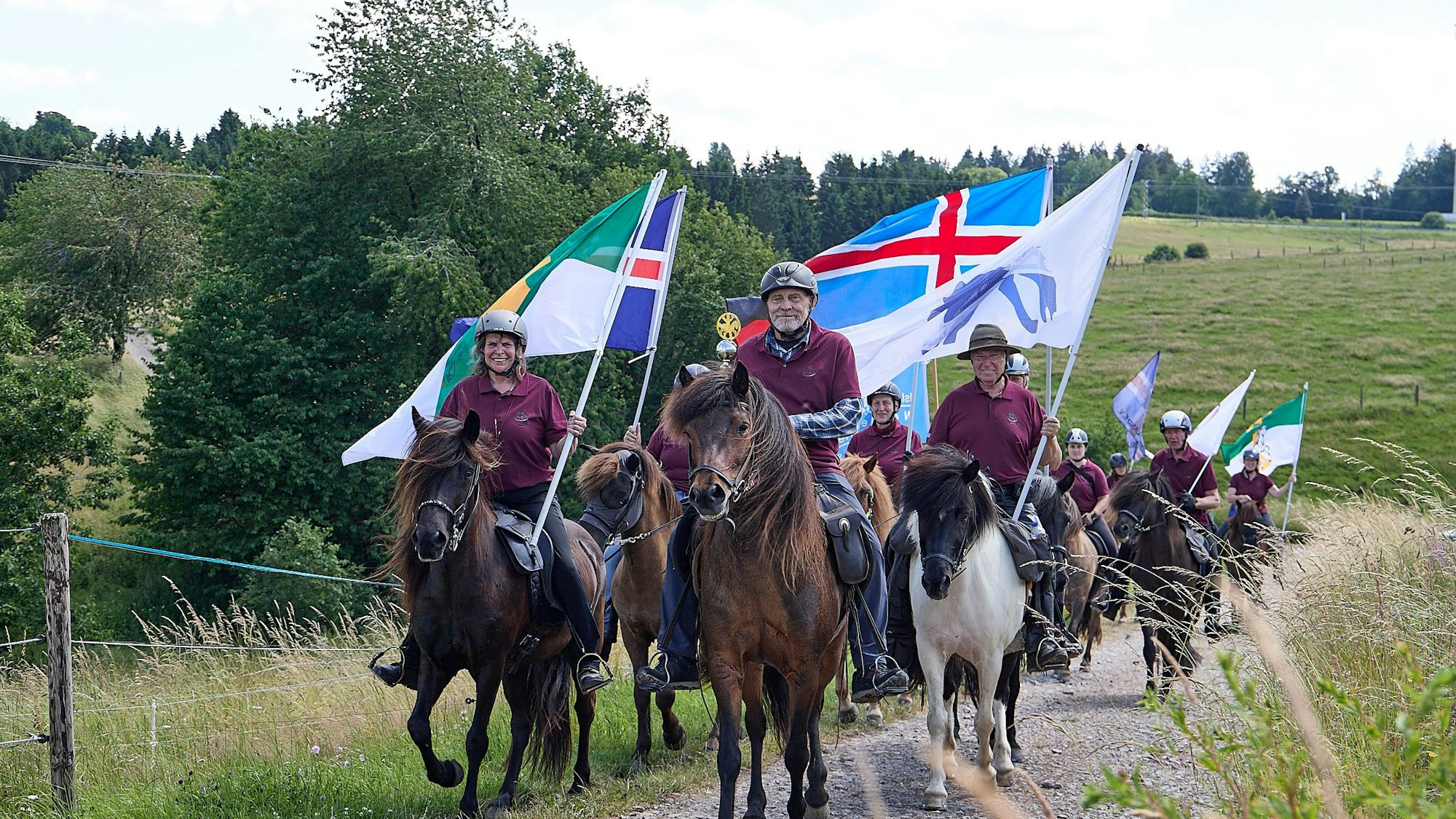 Reiter auf Islandpferden reiten mit Fahnen in der Hand über einen Feldweg