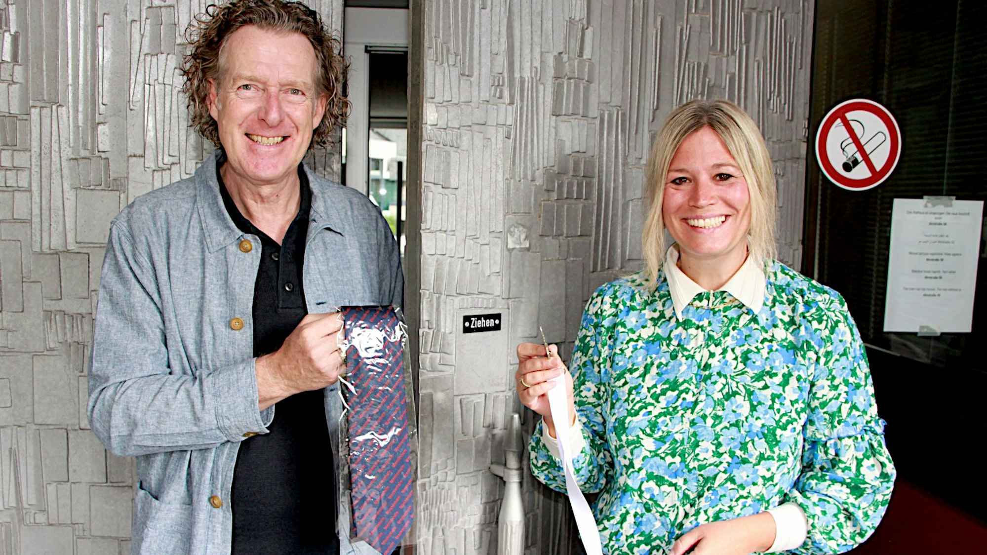 Jennifer Meuren und Boris Enning stehen an der Eingangstür zum Rathaus von Blankenheim. Er hält eine Krawatte in der Hand, sie einen Schlüssel.