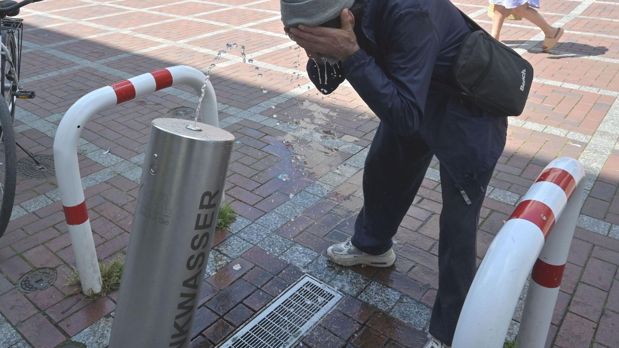 Ein Mann trinkt an einer Trinkwassersäule.