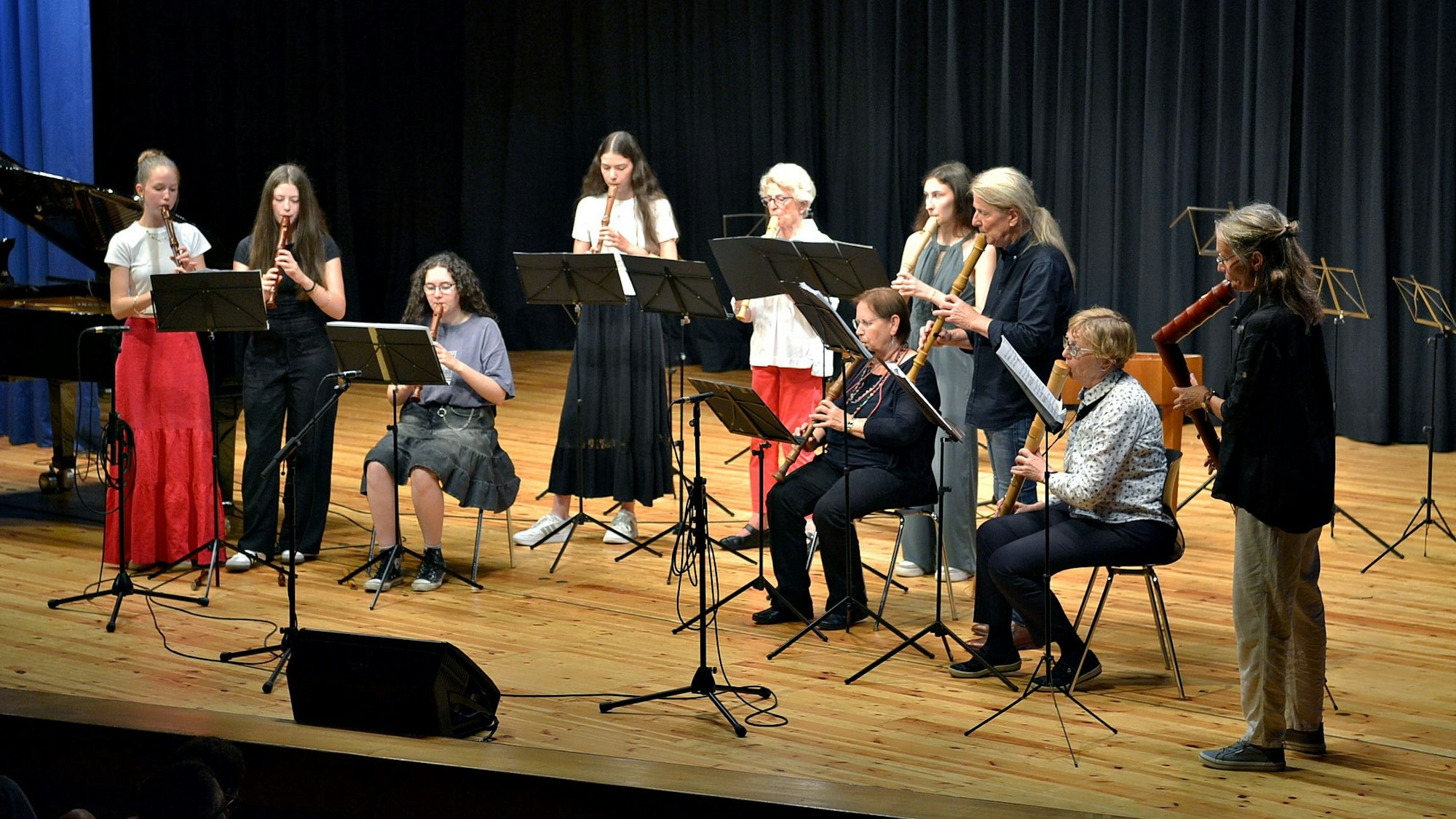 Eine Gruppe von Musikerinnen und Musikern steht auf der Bühne. Sie spielen auf unterschiedlichen Flöten.