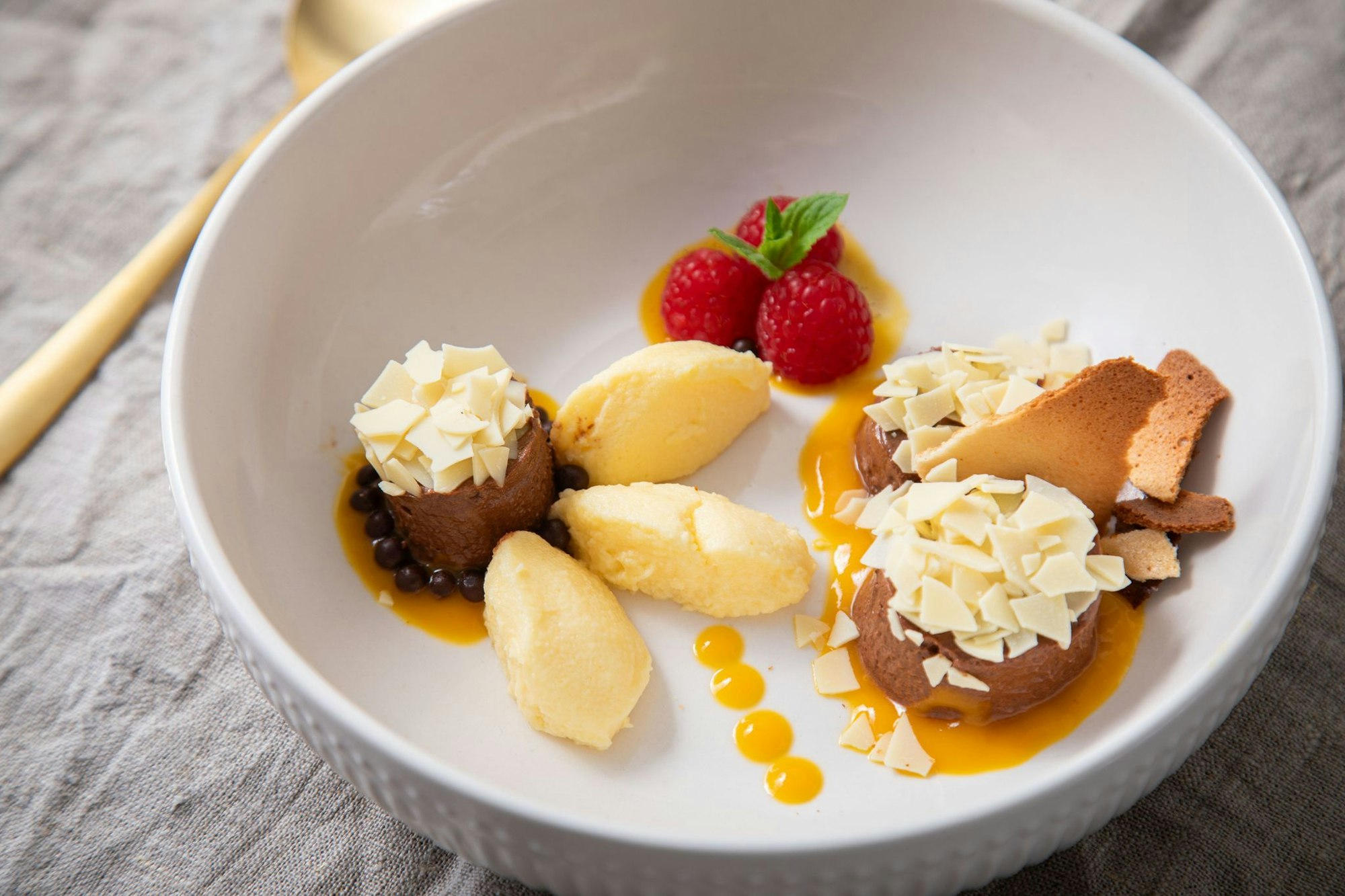 Dessert-Teller mit Schokoladen- und Mango-Mousse auf Mangopüree. Getoppt wird alles mit Eiswaffelsplittern, Schokoraspeln, Himbeeren und Minzblättern.
