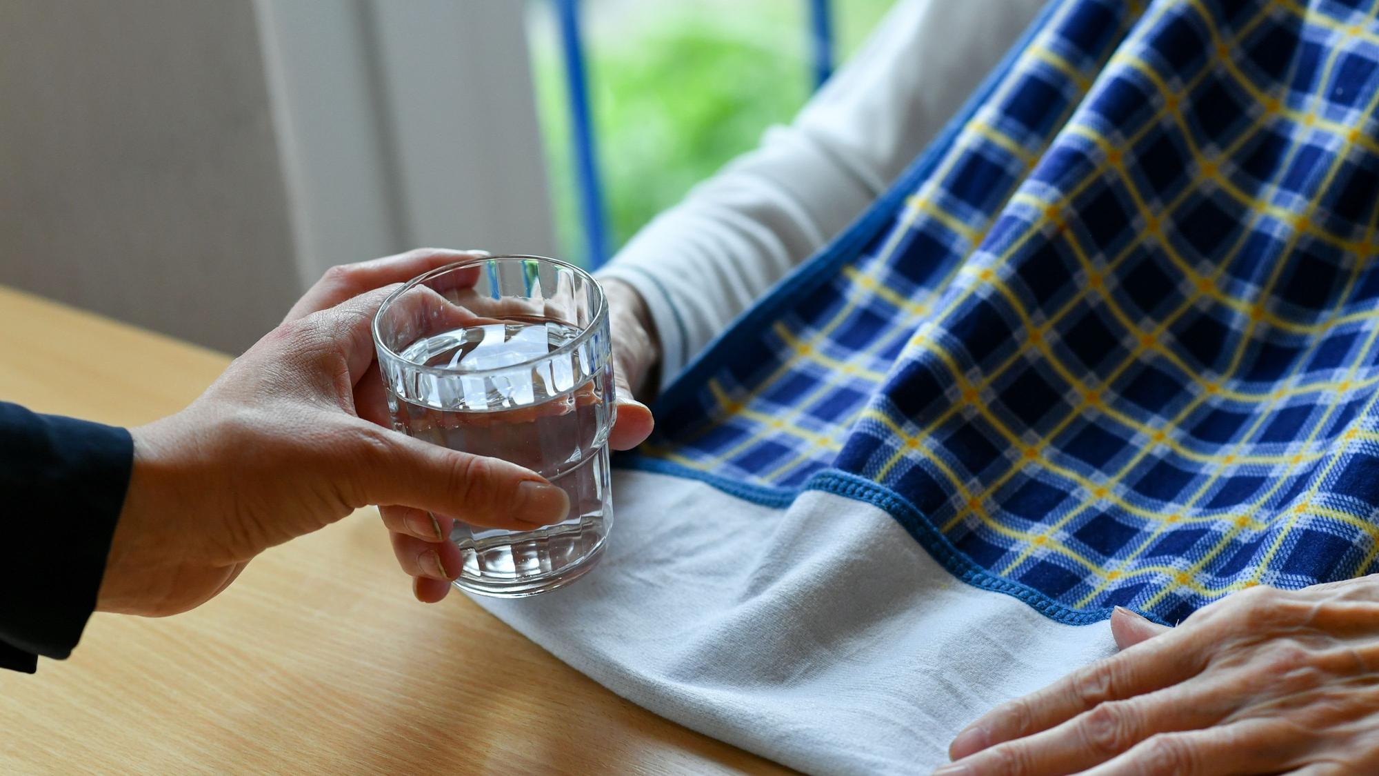 Eine Pflegerin reicht einer alten Frau ein Glas Wasser.