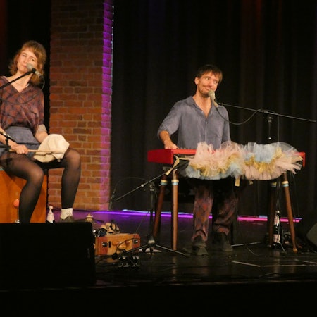 Ein Kabarett-Duo, bestehend aus einer Frau und einem Mann, führt auf einer Bühne ihr Programm vor.