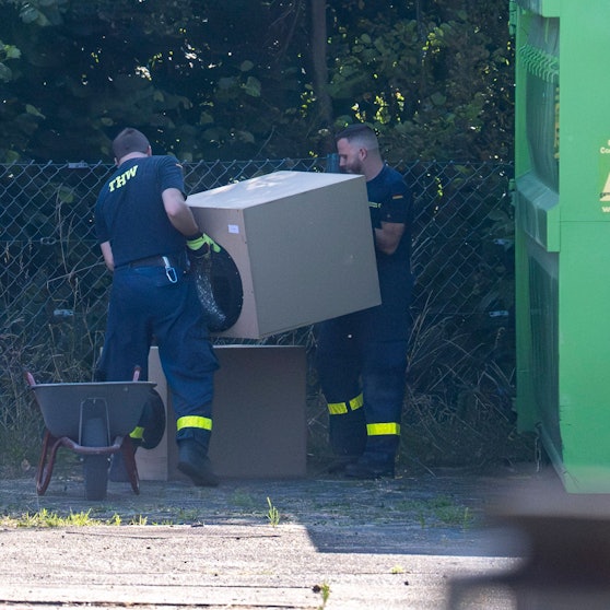 Zwei THW-Mitarbeiter wuchten ein würfelförmiges Bauteil einer Lüftungsanlage aus einer Schubkarre.