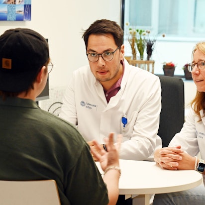 Der Patient ist von hinten zu sehen, er trägt eine schwarze Baseball Cap verkehrt herum auf dem Kopf. Die Ärzte sind mit ihm im Gespräch.