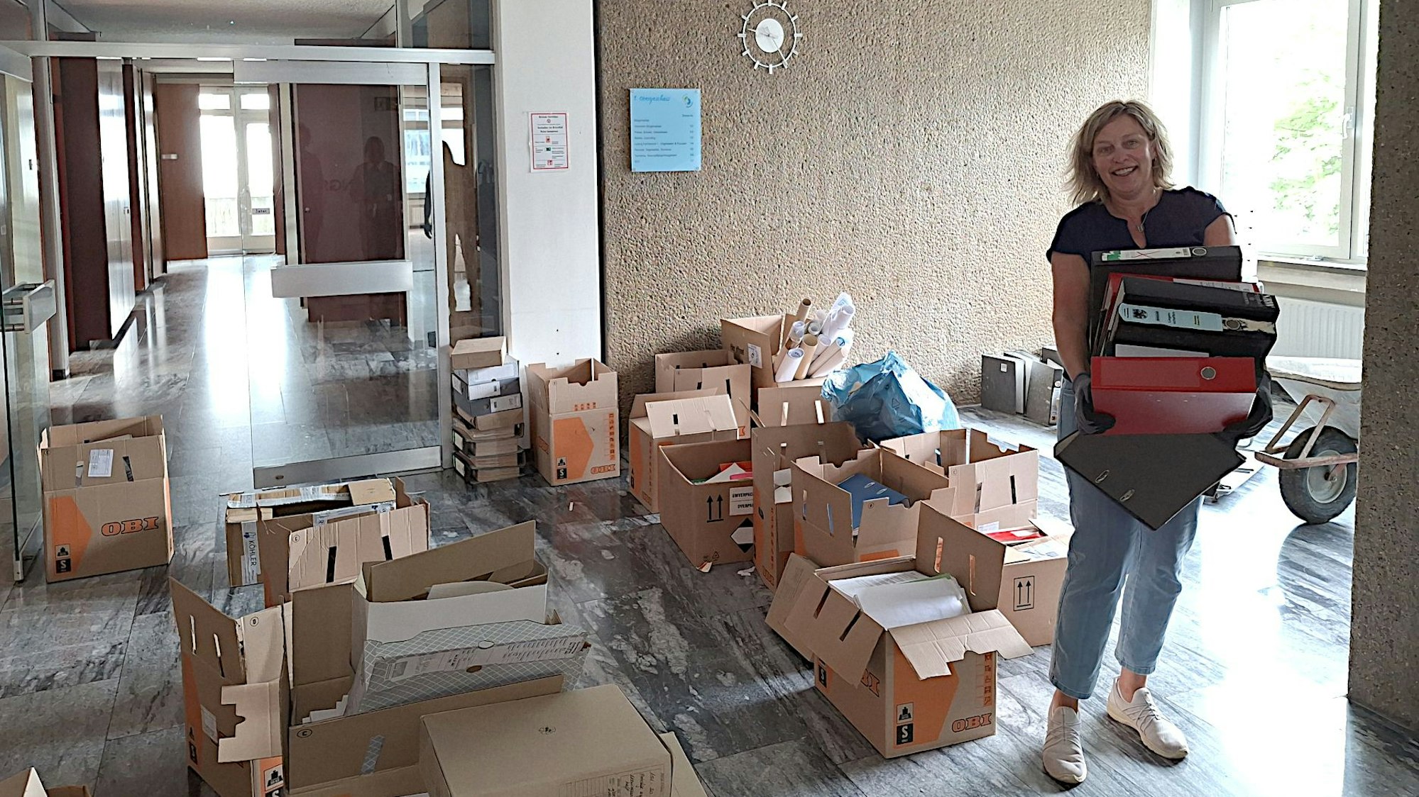 Michaela Bell trägt einige Aktenordner. Um sie herum im alten Rathaus von Blankenheim stehen Umzugskisten.