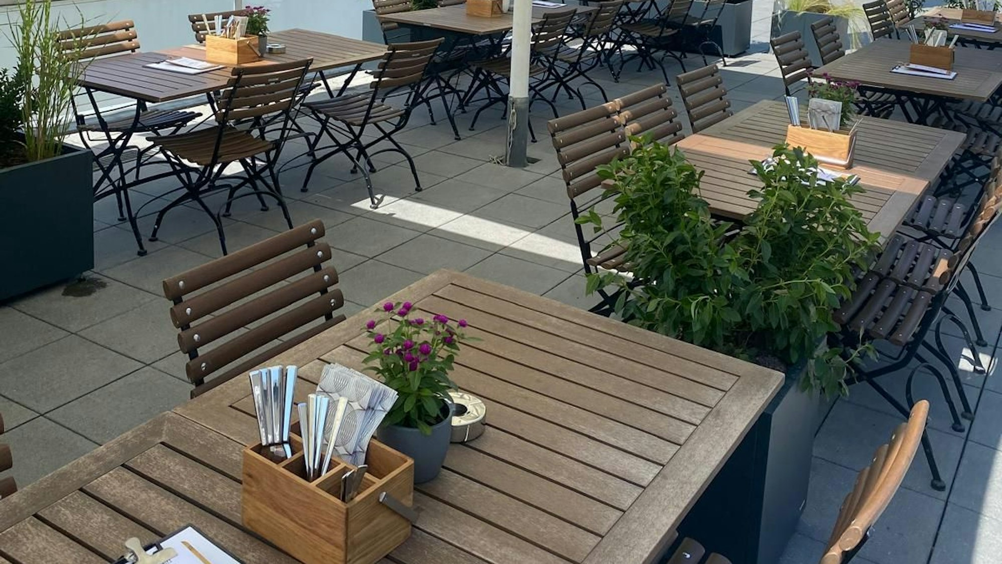 Außenbereich des öffentlichen Restaurants am Geißbockheim mit Tischen, Stühlen und Pflanzen.
