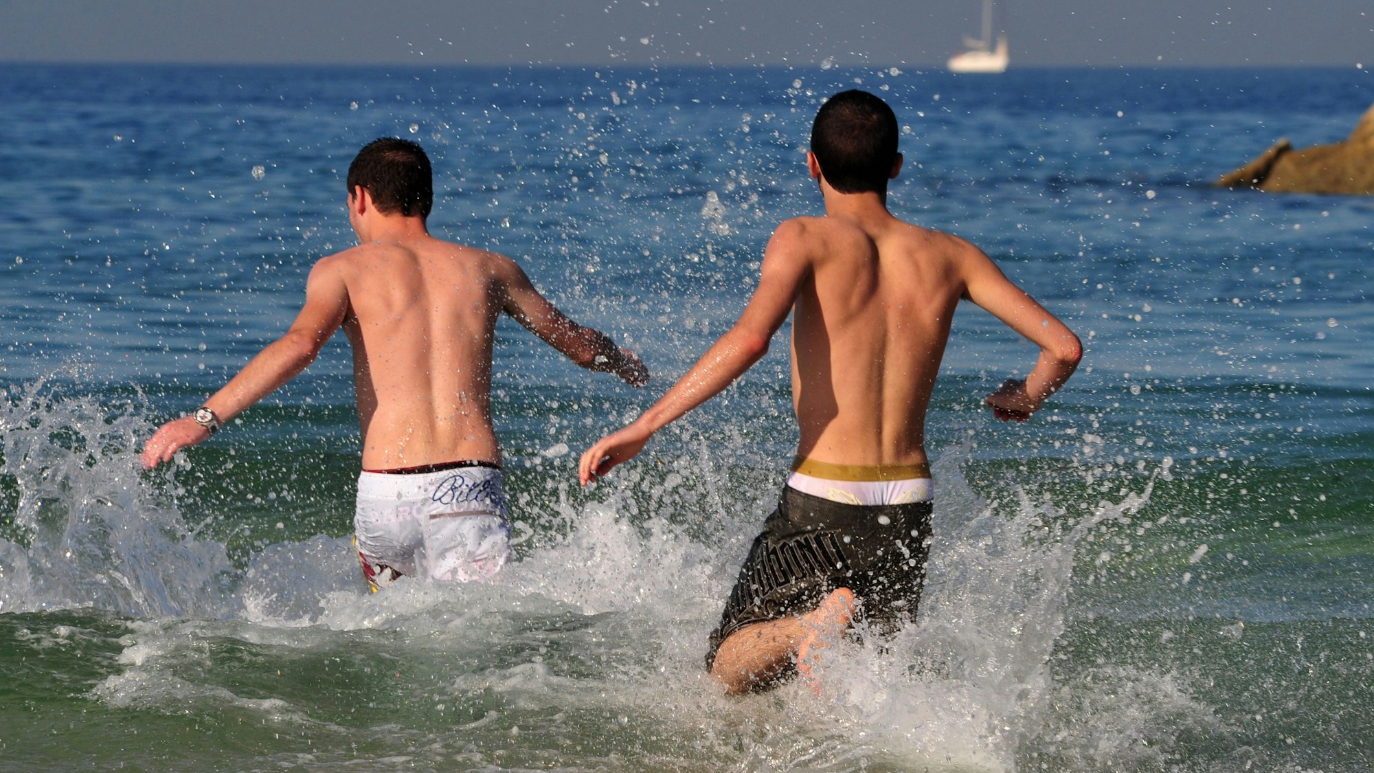 Junge israelische Männer laufen an einem sehr heißen Tag zum Meer.