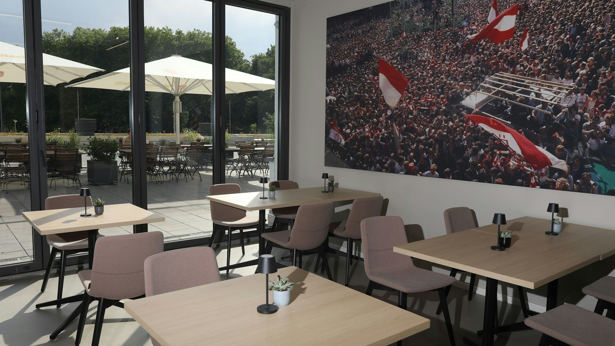 Blick in das umgebaute öffentliche Restaurant mit Außenbereich mit Tischen und Stühlen sowie einem Bild mit FC Fans.
