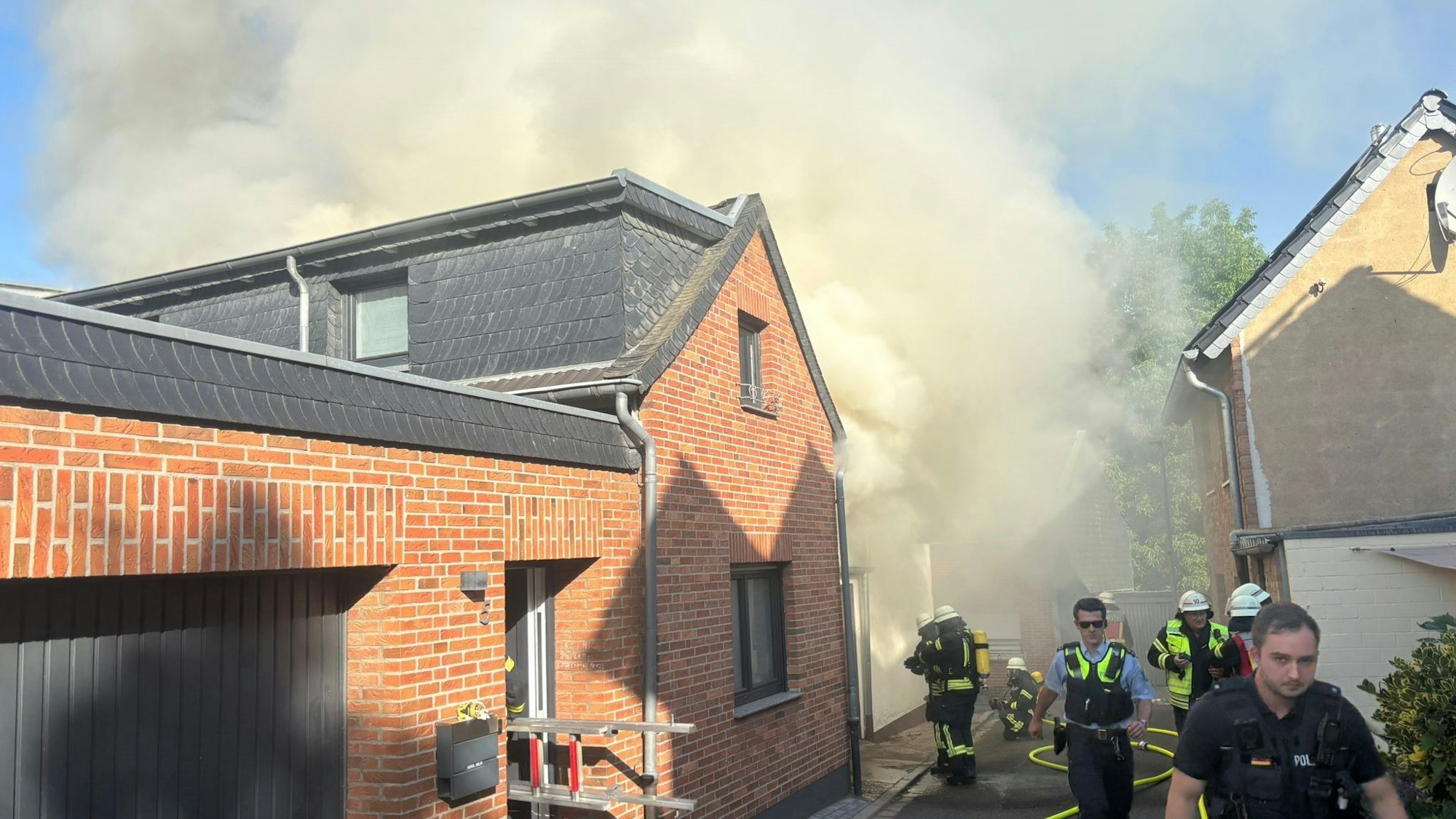 Das Bild zeigt mehrere Einsatzkräfte von Feuerwehr und Polizei an einem qualmenden Gebäude