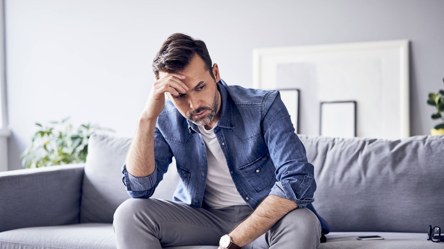 Mann sitzt nachdenklich traurig auf der Couch.