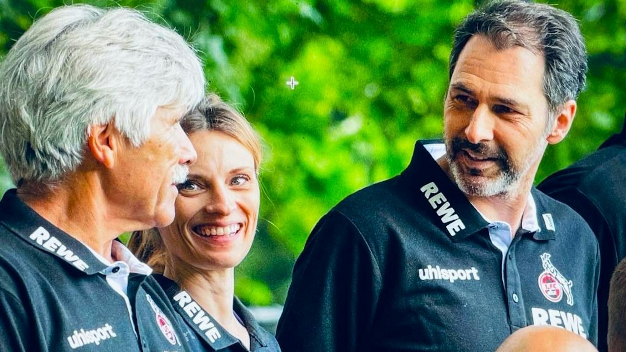 Zwei Männer stehen links und rechts von einer Frau, alle tragen FC-Trikots.