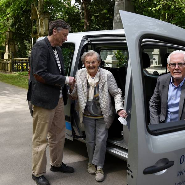 Josef Terfrüchte sitzt im Friedhofsmobil, eine ältere Frau steigt mit der Hilfe eines Mannes aus dem Auto aus.
