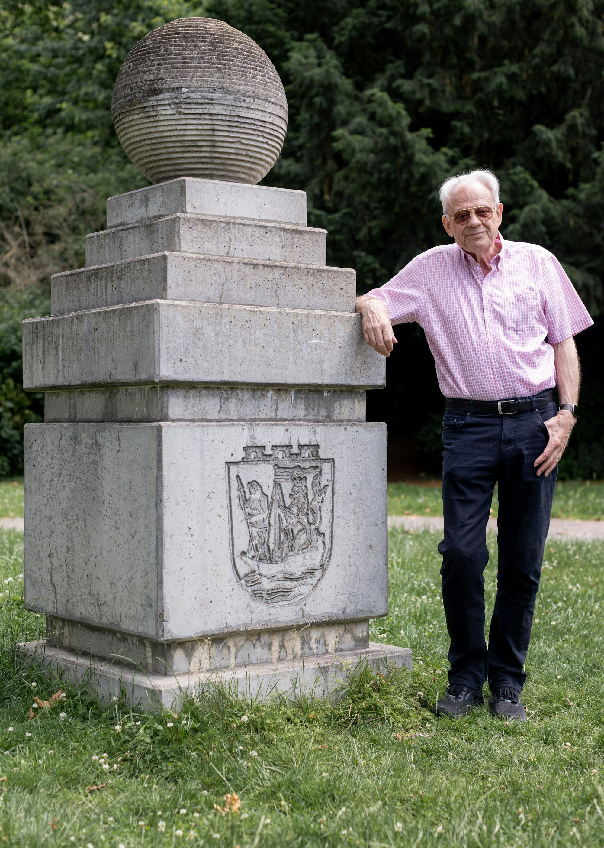 Ein Mann lehnt an einer Steinskulptur, die in einem Park steht.