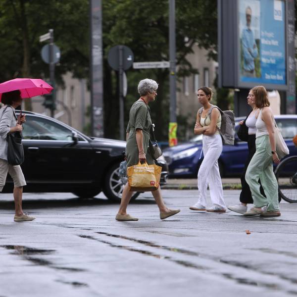 Die Wetterlage schlägt um: Am Sülzgürtel in Köln spazieren Kölnerinnen und Kölner in Sommerkleidung durch den Regen.
