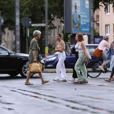 Die Wetterlage schlägt um: Am Sülzgürtel in Köln spazieren Kölnerinnen und Kölner in Sommerkleidung durch den Regen.