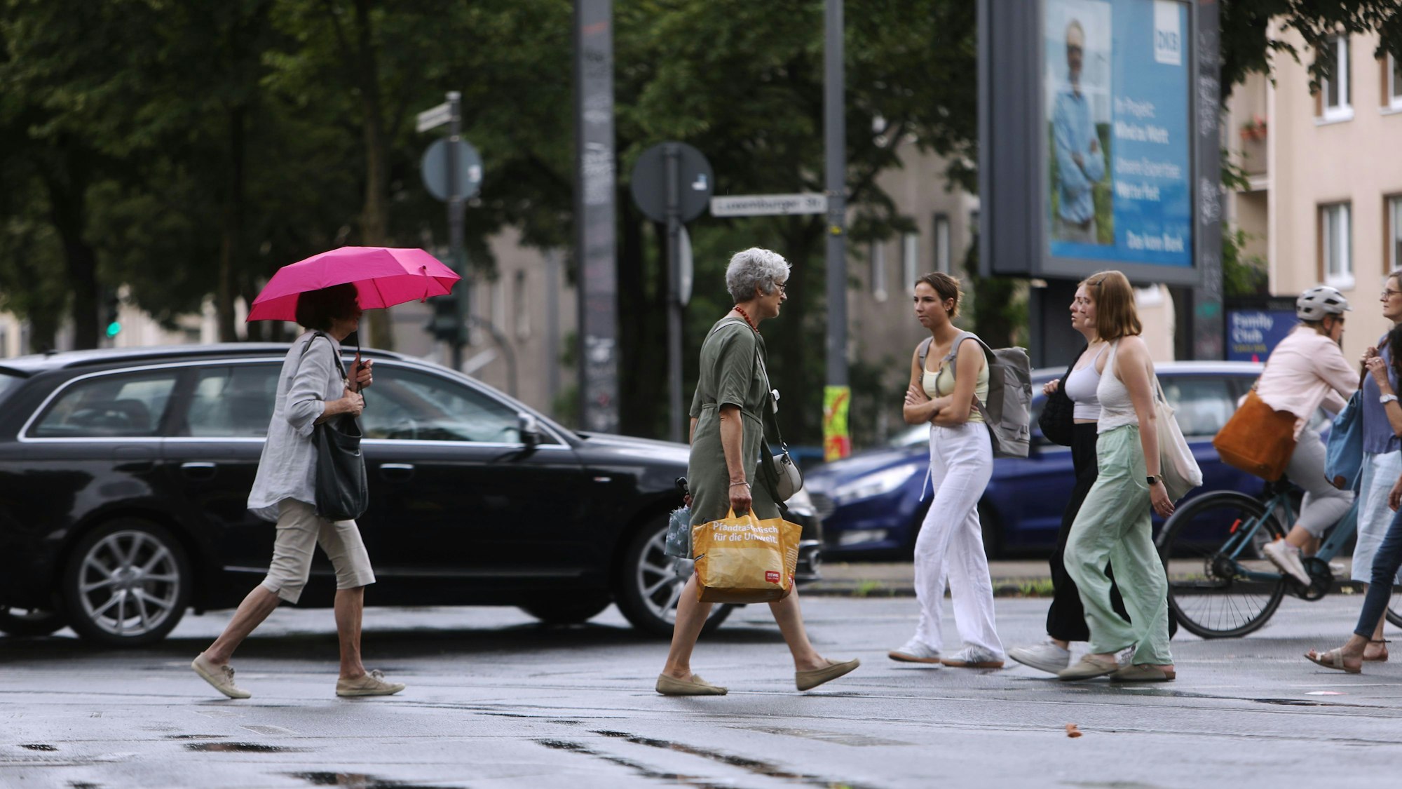 Die Wetterlage schlägt um: Am Sülzgürtel in Köln spazieren Kölnerinnen und Kölner in Sommerkleidung durch den Regen.