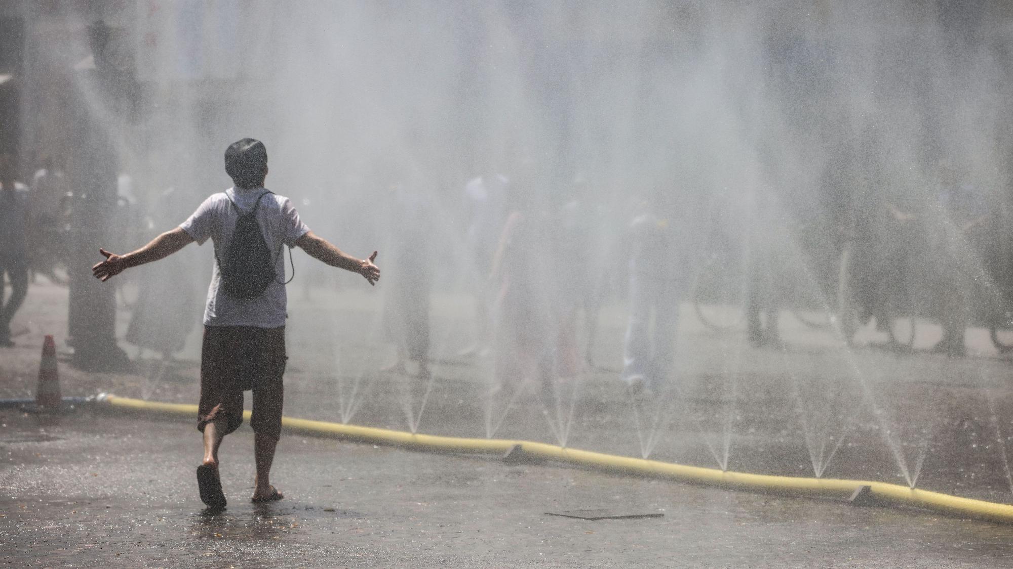 Ein Mann geht durch den Wassernebel in der Südstadt. Unter dem Motto Cooling Cologne hat die Stadt Köln für eine Abkühlung Schläuchen bereit gestellt, die feinen Wassernebel versprühen.