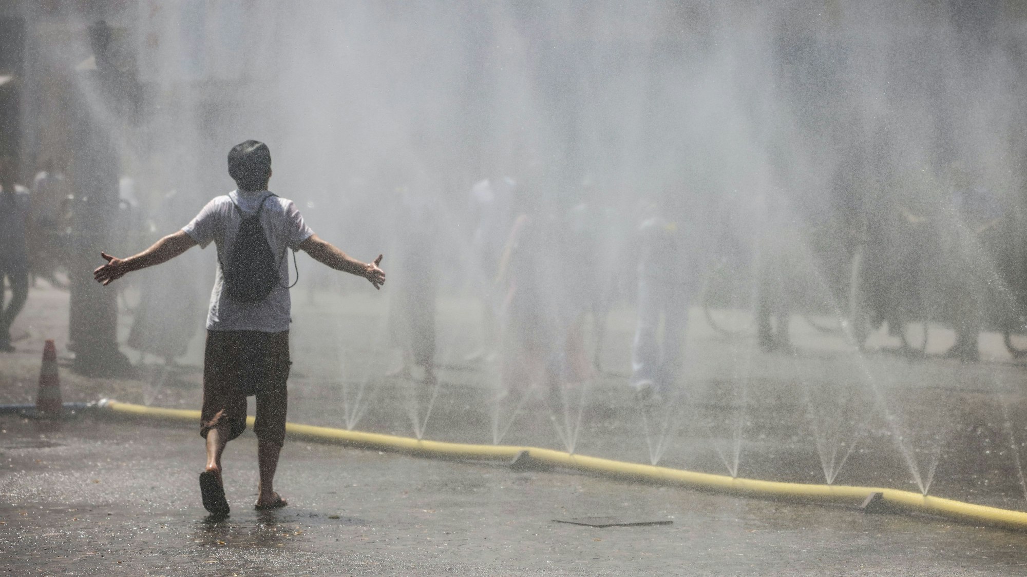 Ein Mann geht durch den Wassernebel in der Südstadt. Unter dem Motto Cooling Cologne hat die Stadt Köln für eine Abkühlung Schläuchen bereit gestellt, die feinen Wassernebel versprühen.