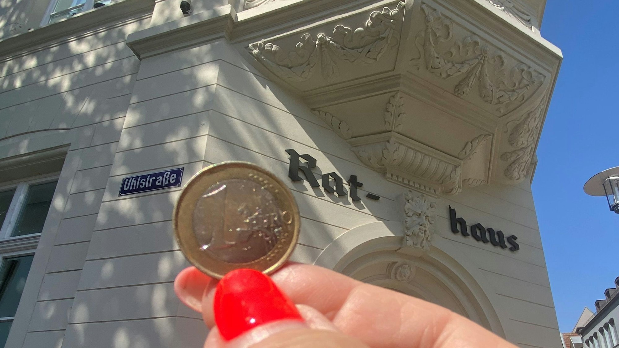 Zu sehen ist eine Ein-Euro-Münze und im Hintergrund das Brühler Rathaus.