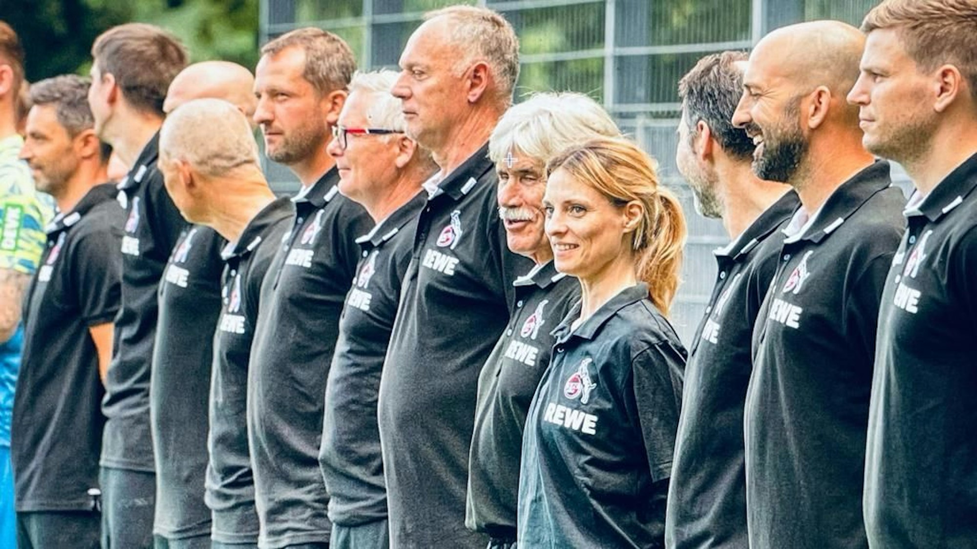 Nebeneinander stehen viele Männer, mittendrin eine Frau mit Pferdeschwanz.